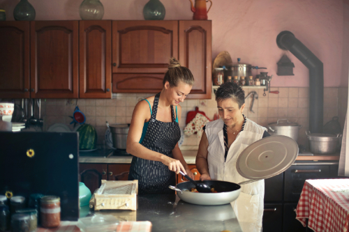 mother wearing white sleeveless blouse and daughter wearing light blue tank top cooking together and talking in the kitchen